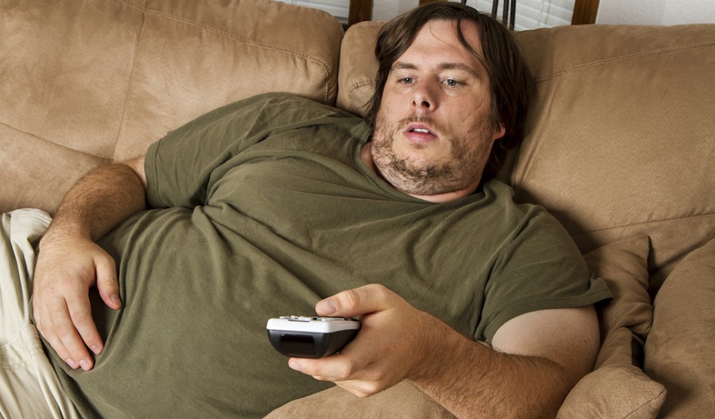 Overweight guy sitting on the couch with remote in hand trying to watch some TV.